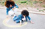 Mother and daughter using chalk to draw colourful circle on pathway