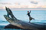 Woman standing on large driftwood tree trunk on beach