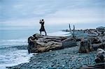 Woman looking through binoculars from large driftwood tree stump on beach