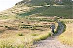 Rear view of young male runner running up hillside track