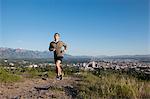 Young male runner running along track above city in valley