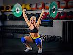 Young woman squatting with barbell raised in gym