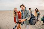 Group of friends walking along beach, young couple looking at smartphone