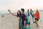 Group of friends walking along beach, young couple taking self portrait with smartphone