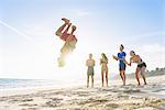 Group of friends on beach watching friend do somersault