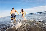 Young couple running in sea, rear view