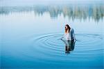 Young woman standing in middle of lake ripples looking down