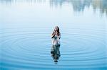 Young woman standing in lake ripples praying with eyes closed