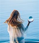Rear view of young woman with long red hair standing in lake holding crystal ball