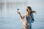 Young woman with long red hair standing in lake gazing at crystal ball