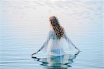 Rear view of young woman standing in lake rippling surface with her fingers