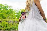 Cropped shot of young woman wearing white dress carrying bunch of flowers behind her back