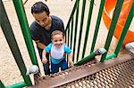 Young man guiding toddler brother up playground slide steps