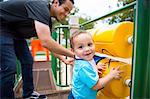 Young man playing with toddler brother on playground equipment