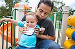 Young man guiding toddler brother on playground slide