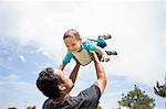 Young man playing lifting up toddler brother in park