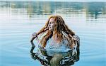 Head and shoulders of beautiful young woman with long red hair in lake