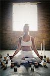 A blonde woman sitting on the floor on a yoga mat, circled by lit candles.