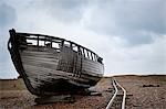 Abandoned wooden boat beached on the shingle near old narrow gauge rails.