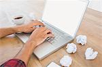 Hands typing on a laptop with paper pellets beside
