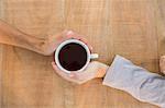 Two hands holding a cup of coffee on wooden table