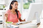Creative businesswoman eating a salad and working on computer