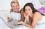 Portrait of smiling homosexual couple lying and using laptop