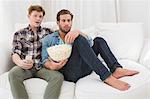 Homosexual couple eating pop corn on sofa