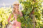 Smiling woman wearing straw hat and standing next to grapevine