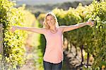 Portrait of smiling blonde woman standing in front of grapevine with arms outstretched