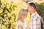 Man kissing his woman on forehead with eyes closed next to grapevine