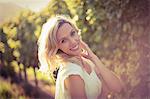 Portrait of smiling blonde woman standing next to grapevine