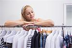 Pretty blonde smiling at camera by clothes rail