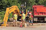 Construction workers watching excavators digging hole on watermain project