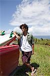 Young man leaning against surfboard in car, portrait