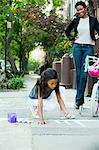 Mother watching daughter draw on sidewalk