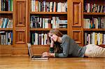 Young woman using laptop by bookshelves