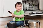 Upset baby on floor with saucepans and wooden spoon