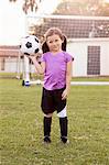 Portrait of girl football player holding up football on practice pitch