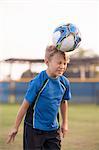 Boy with eyes closed heading football on practice pitch