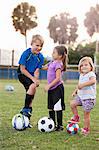 Boy and younger sisters with footballs on practice pitch