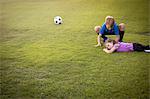 Boy tending injured younger sister on football practice pitch