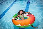 Girl sitting in inflatable ring in swimming pool looking at camera smiling