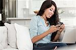 Young woman, relaxing on sofa, laptop on lap, holding smartphone