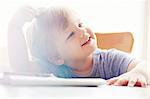 Boy sitting at table scratching head, looking away smiling