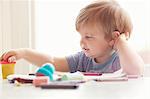 Boy sitting at table leaning on elbow looking at art supplies