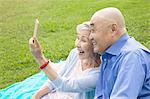 Senior couple sitting in park, taking self portrait using smartphone