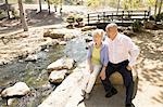 Senior couple sitting on rock beside stream