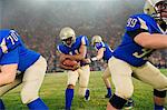 Team of teenage American football players playing on stadium pitch