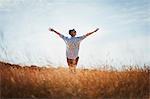 Exuberant senior woman with arms outstretched in sunny field